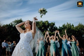 Hungary is the backdrop for a joyful bride throwing her bouquet mid-air under a bright blue sky, capturing the excitement and laughter of the tradition for her waiting guests.